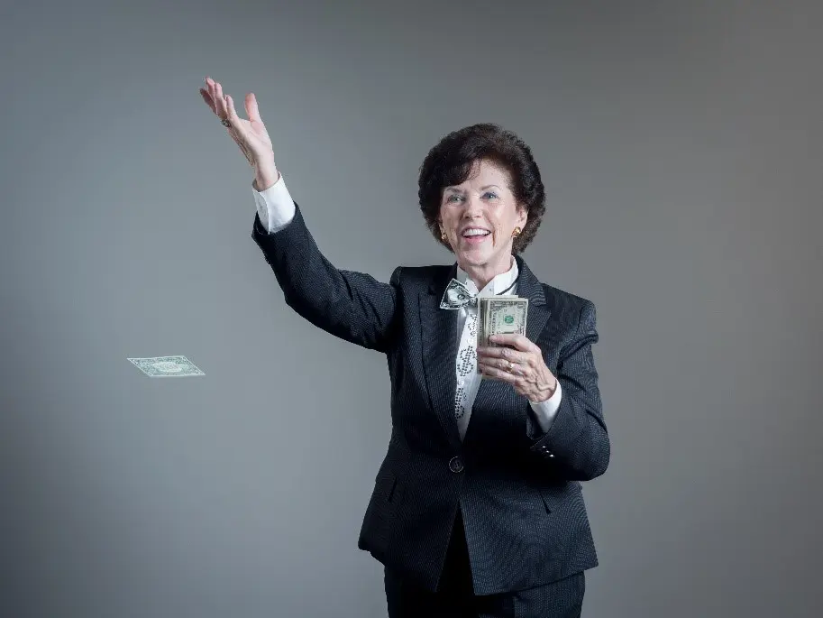 A woman in a suit holding up her hand while smiling.